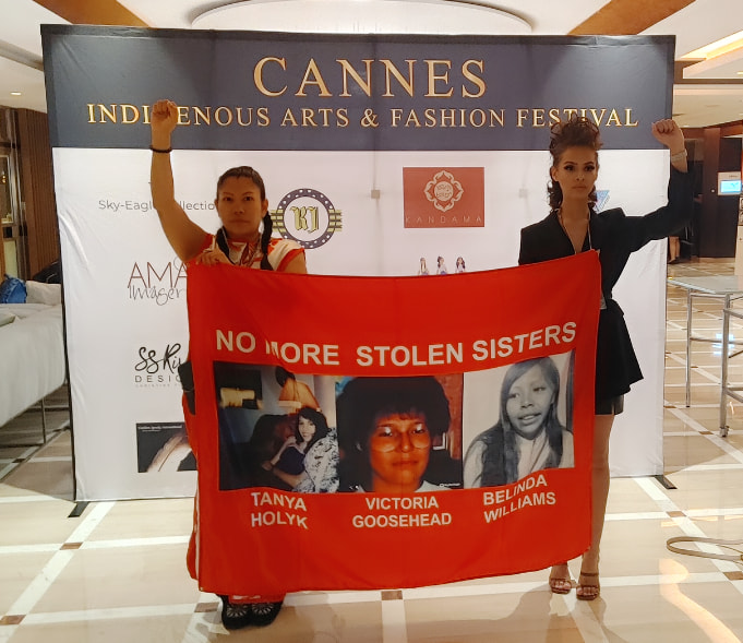 Two women stand holding a poster with images of MMIWG
