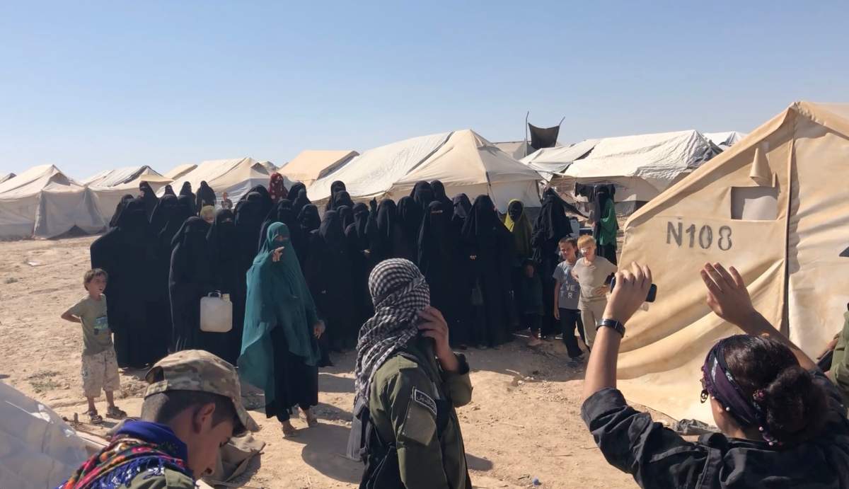 Female YPJ guard at Al-Hol camp for ISIS families in Syria tries to quell protest as woman in green shouts about 'jihad,' 2019.