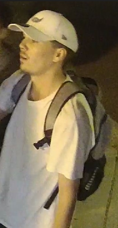 Surveillance image of a suspect in a white cap, white shirt and wearing a backpack.