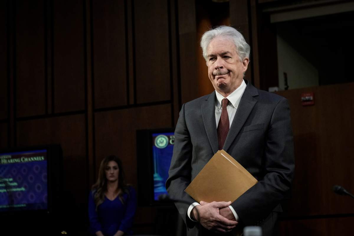 William Burns wearing a suit and holding a manila envelope.
