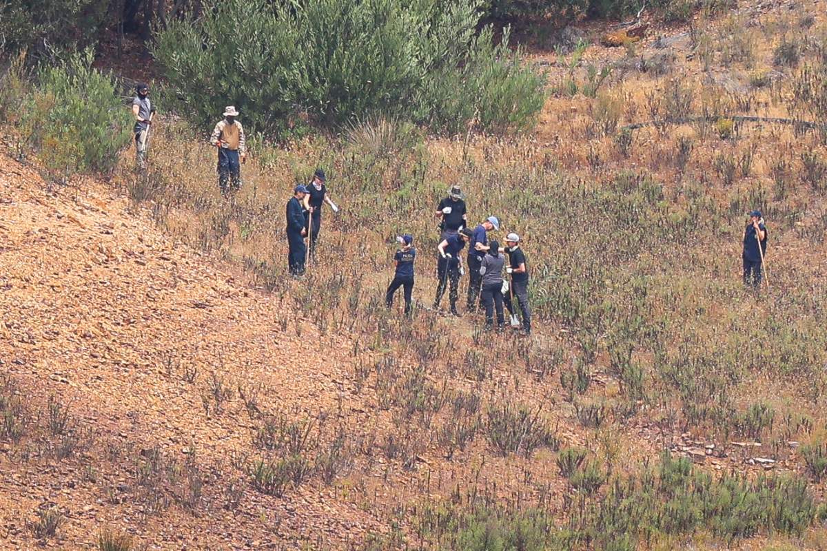 Police stand in a grassy field. It is an aerial shot.