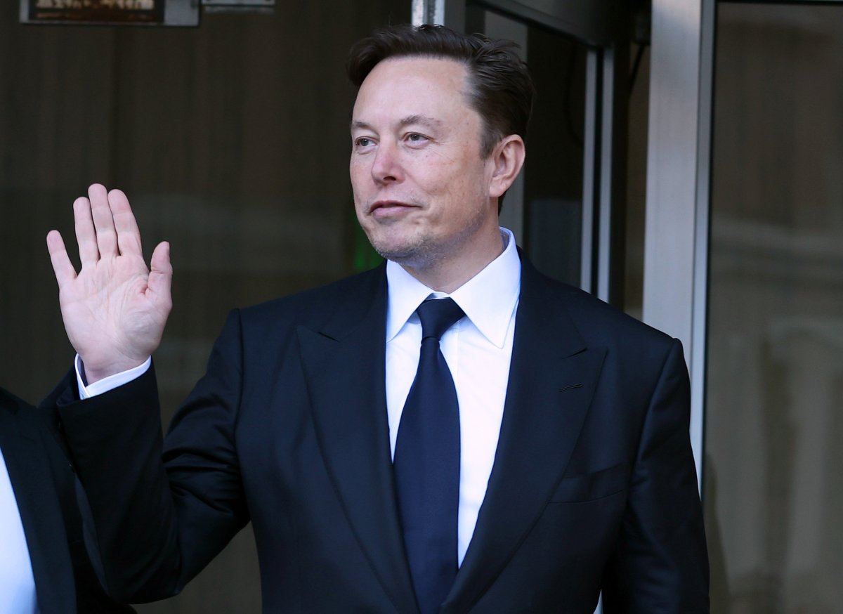 Elon Musk in a suit. He is waving.