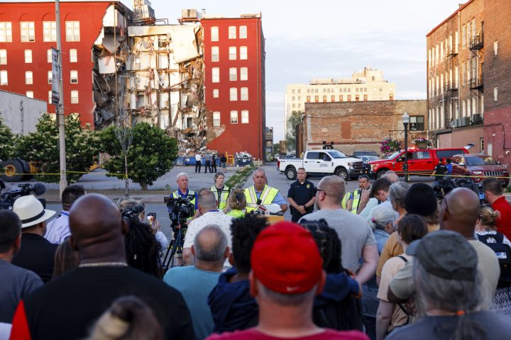 A multi-storey apartment building sits with a section missing, exposing units inside, following a partial collapse of the structure