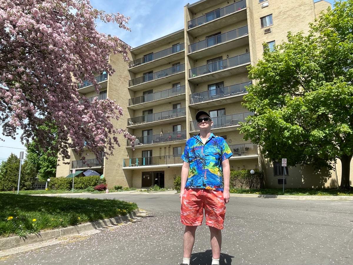 A man stands in front of an apartment building on a sunny day.