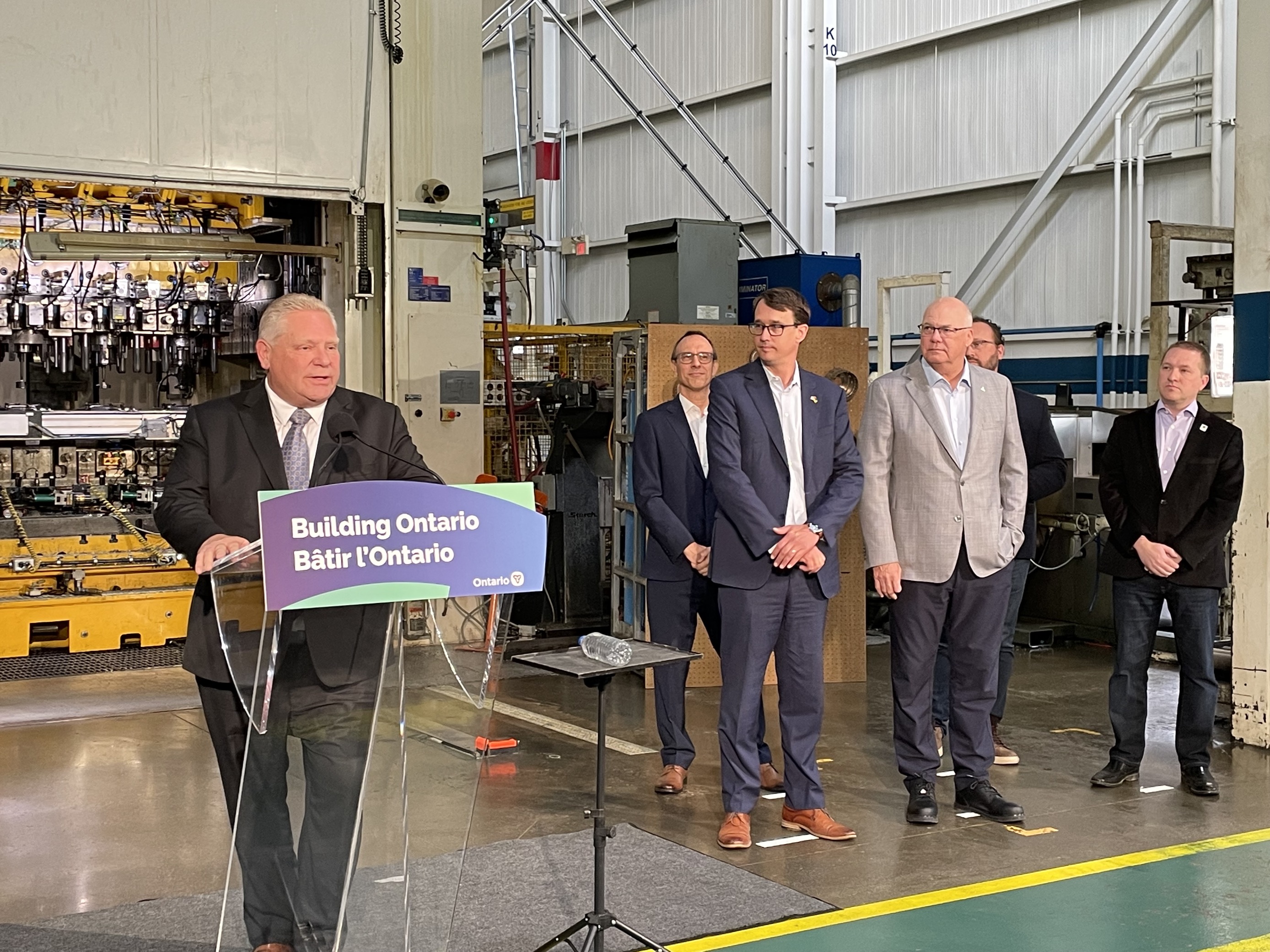 Premier Doug Ford stands at a podium while other politicians stand to his right at a manufacturing facility in London, Ont., on May 24, 2023.