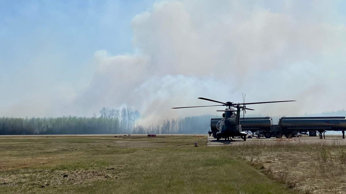 Helicopters wait on the ground while smoke rises in the distance in Rainbow Lake, Alta., Saturday, May 6, 2023.