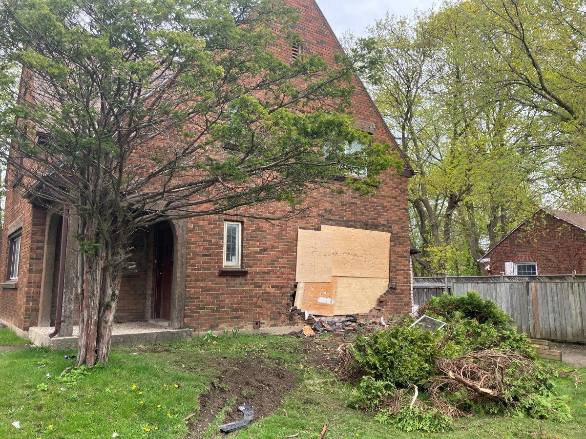 A brick house boarded up with wood after a car crashed into it.