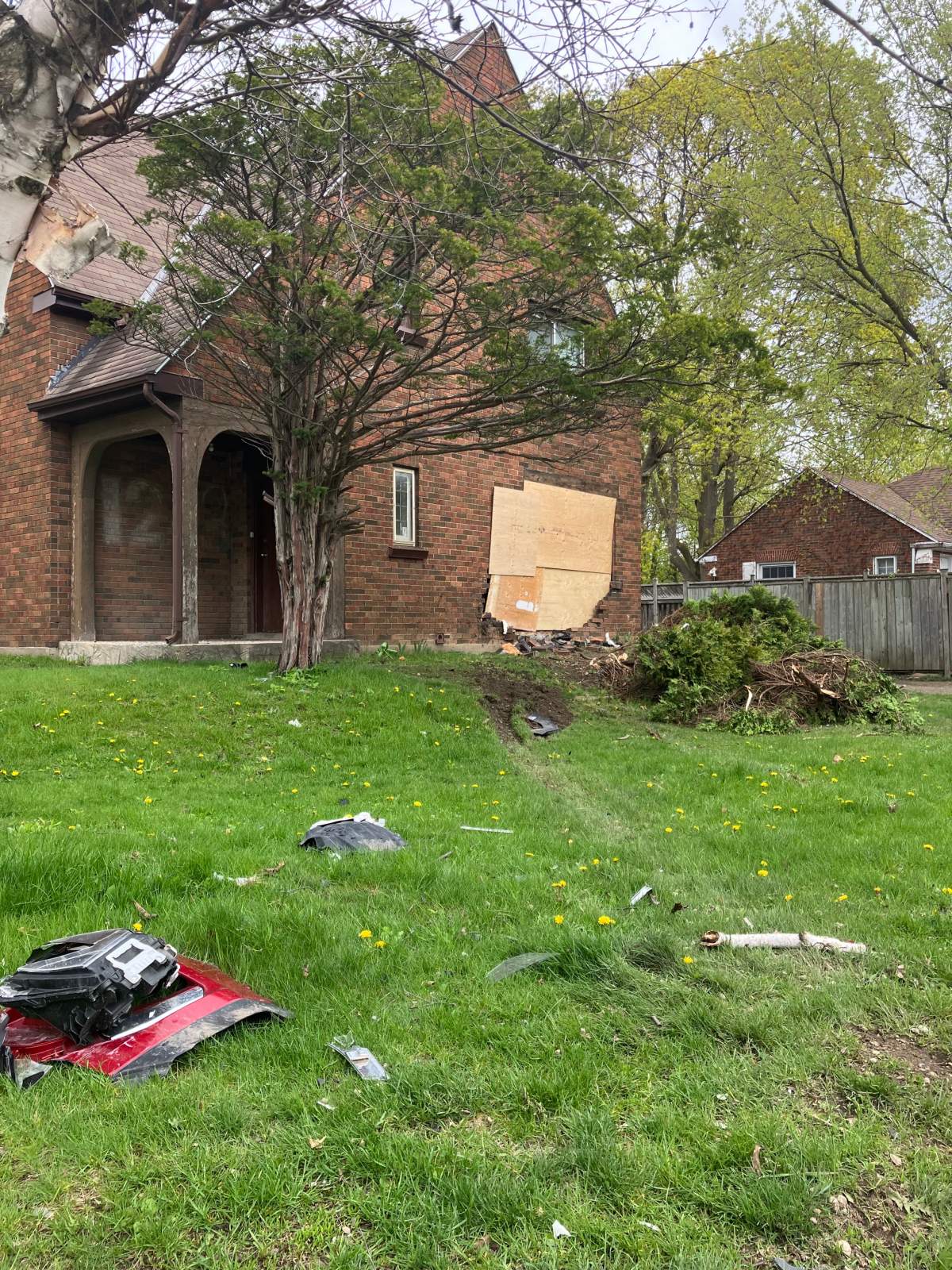 Debris from a car crash is seen in front of a home boarded up with plywood.