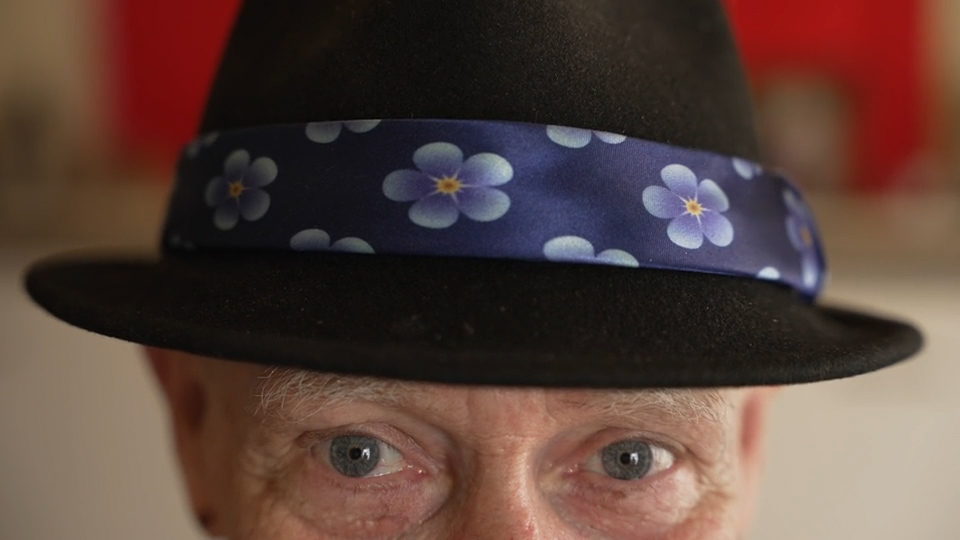 Paul Lea showing us his hat, which is decorated with forget-me-not blue fowers, a symbol associated with dementia