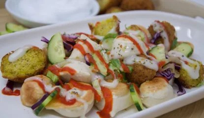 Bite-sized perogies are topped with falafel, sautéed onions, lettuce, red cabbage and sliced cucumbers; all drizzled with a garlic sweet sauce and sriracha.