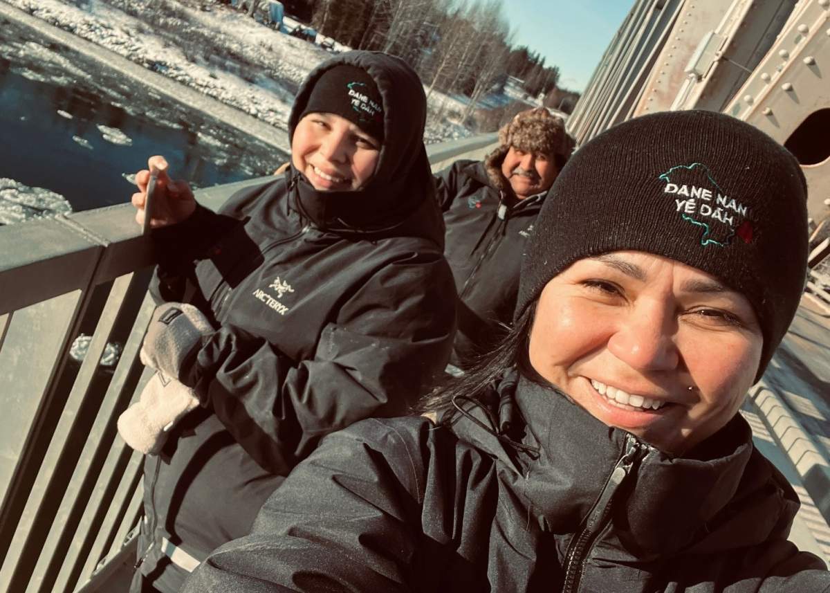 Three people pose for a selfie on a bridge, they're wearing winter clothes.