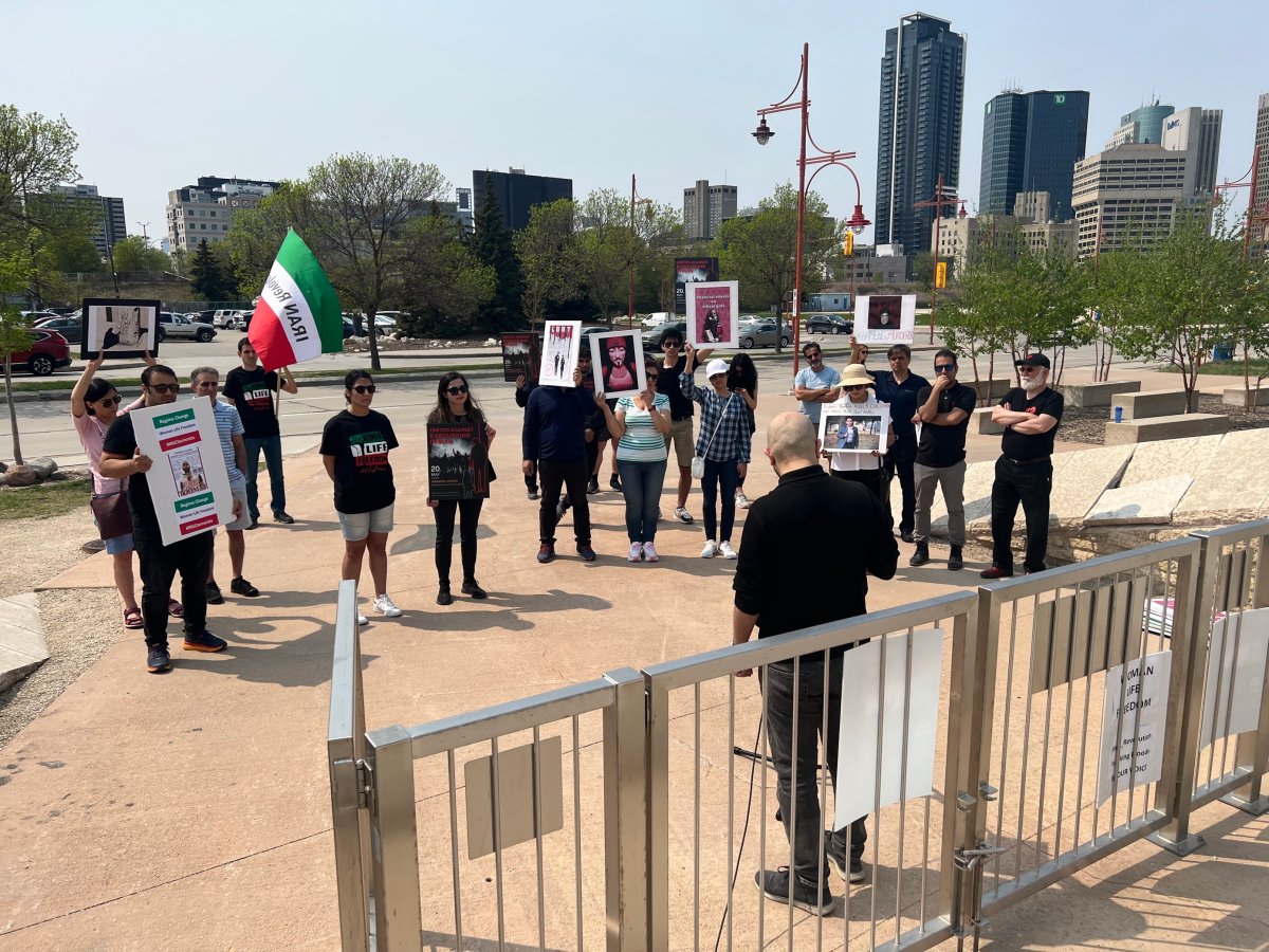 A group of people holding signs and an Iranian flag watch a speaker outside the Canadian Museum for Human Rights