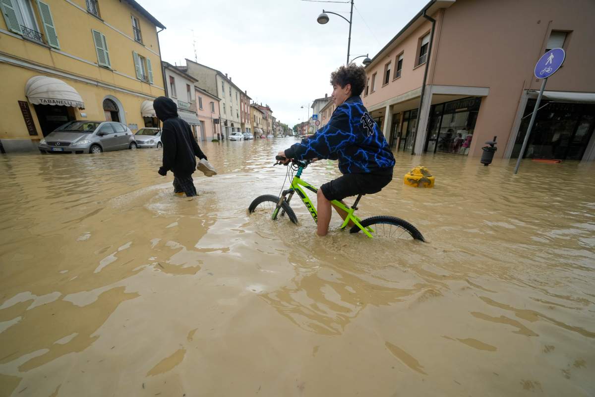 A boy rides through a flooded street in the village of Castel Bolognese, Italy, Wednesday, May 17, 2023. (AP Photo/Luca Bruno)