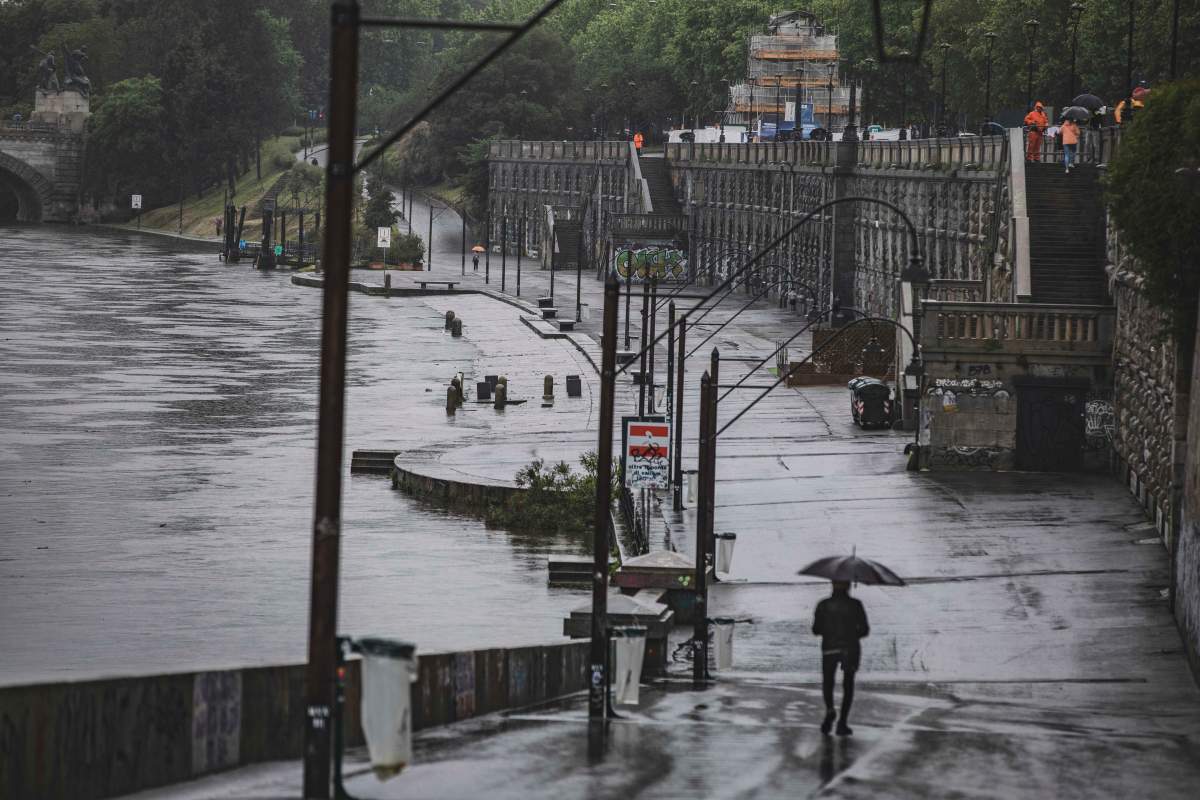 A man walks under heavy rain on the riverside of the Po river in Turin, Italy, Saturday, May 20, 2023. (Andrea Alfano/LaPresse Via AP)