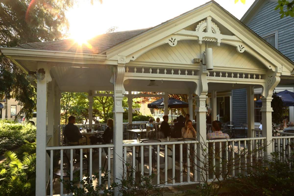 An outdoor dining space surrounded by greenery with the sun shining in the background.