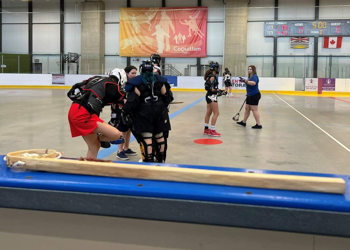 A traditional lacrosse stick lays on the edge of a lacrosse box.