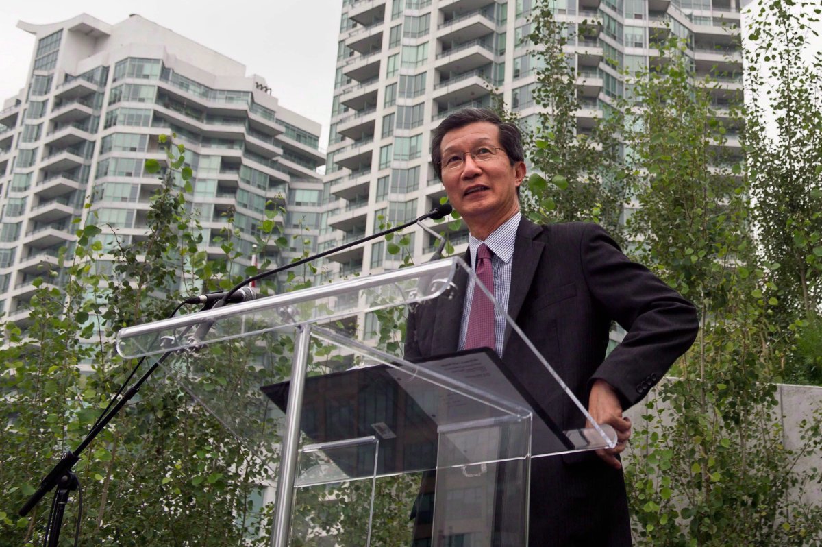 Michael Chan stands at a glass podium in front of a condo tower.