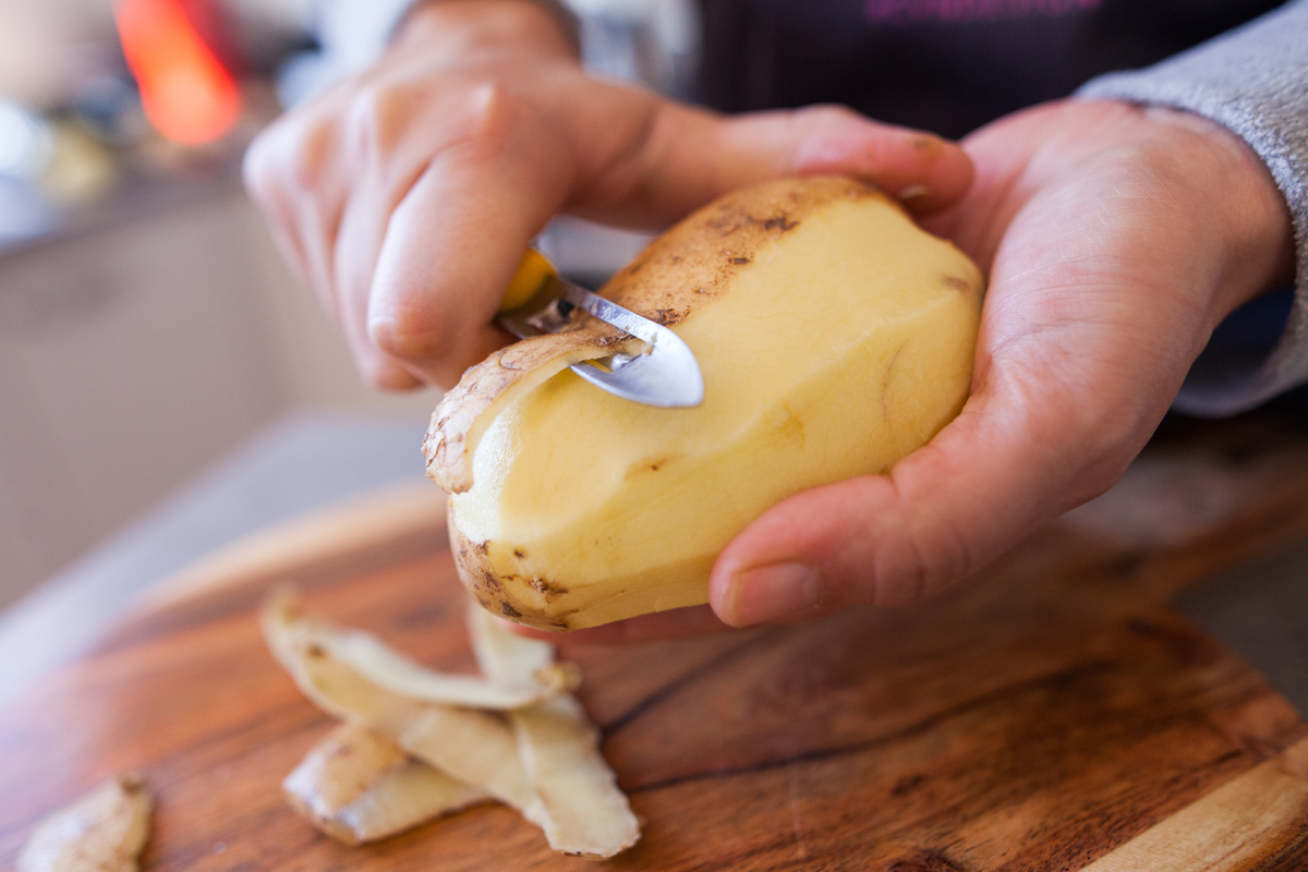 A photo of a person peeling potatoes.