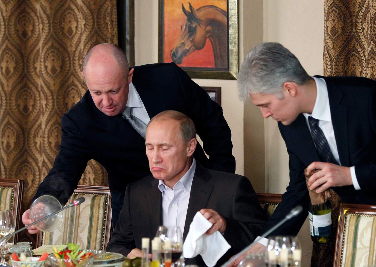 FILE – In this Friday, Nov. 11, 2011 file photo, businessman Yevgeny Prigozhin, left, serves food to Russian Prime Minister Vladimir Putin, center, during dinner at Prigozhin’s restaurant outside Moscow, Russia. (AP Photo/Misha Japaridze, Pool, File)