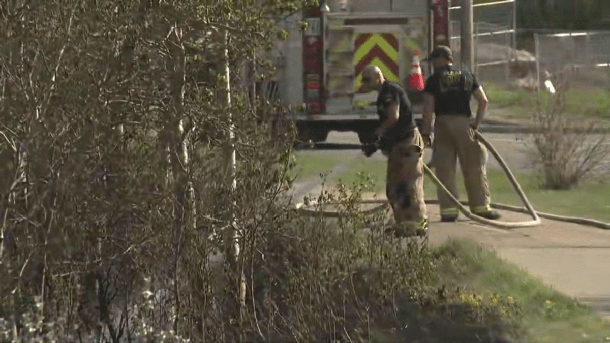 Firefighters spray down a brushfire in southwest Calgary on May 19, 2023.