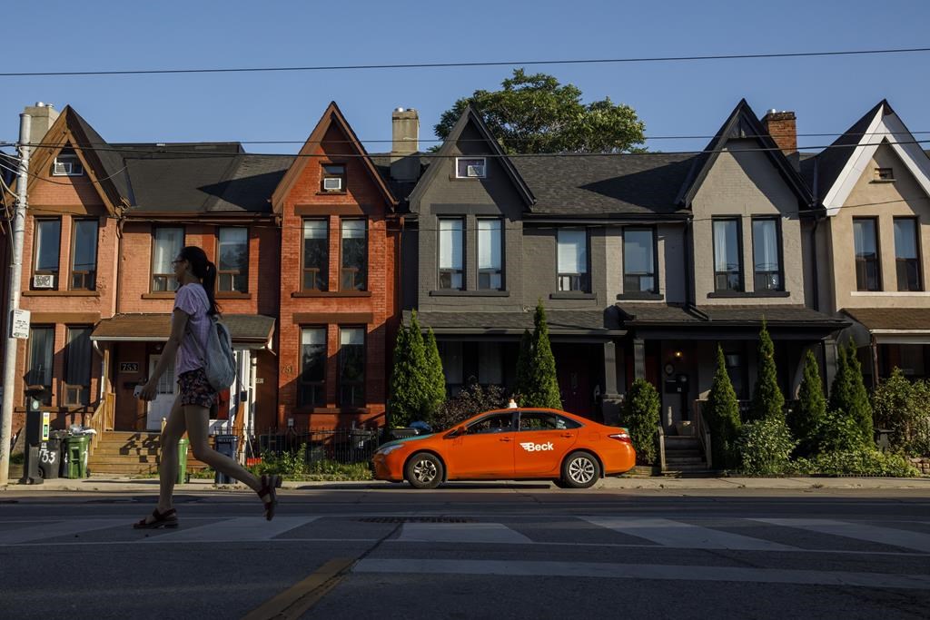A person walks by a row of houses in Toronto on Tuesday July 12, 2022. A new policy allowing single family homes to be converted into low-rise multiplexes in Toronto is being hailed by observers as a welcome move, although experts warn it won't make housing more affordable in Canada's most populous city right away. THE CANADIAN PRESS/Cole Burston.