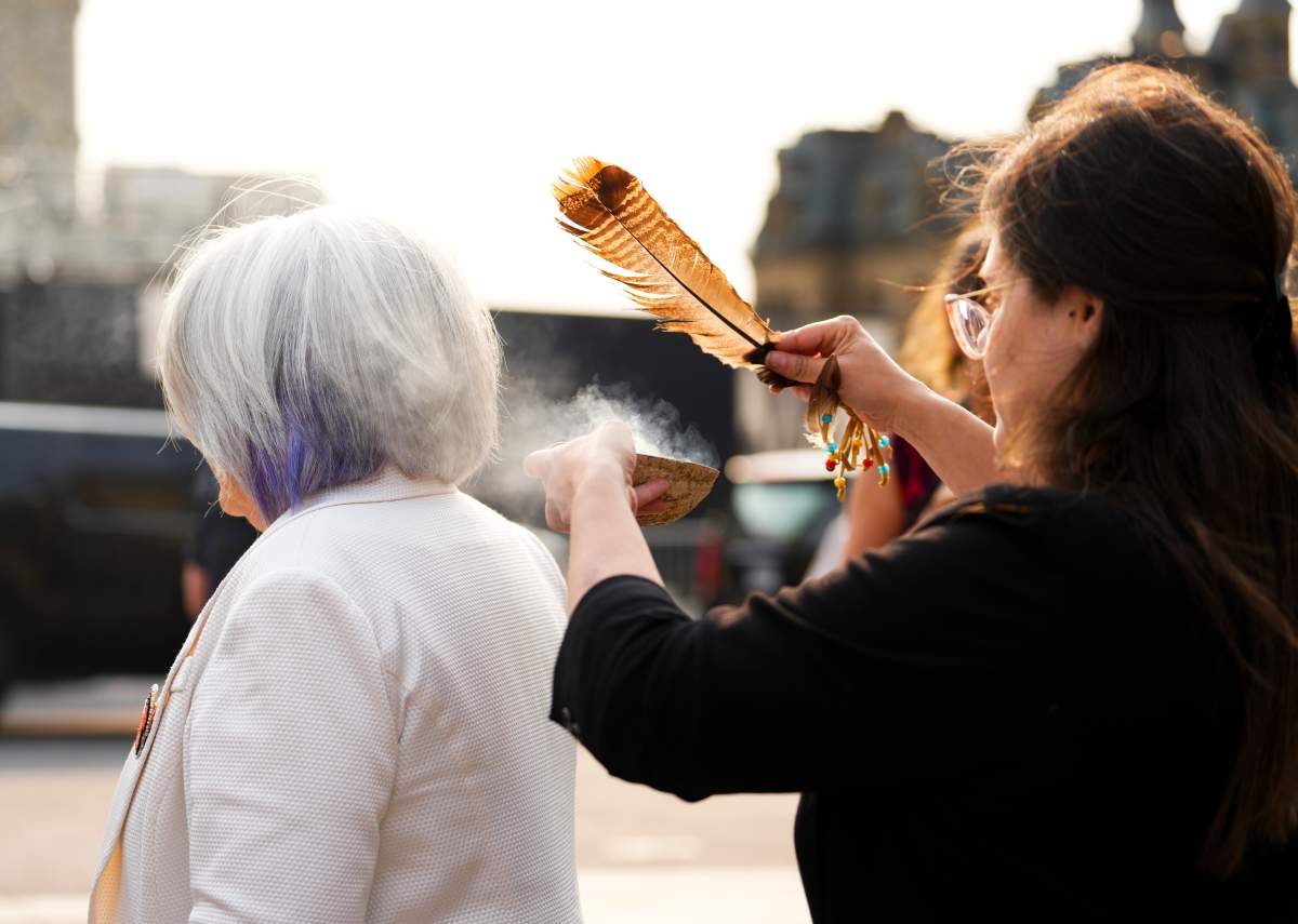 A woman stands as a feather and smoke are wafted towards her.