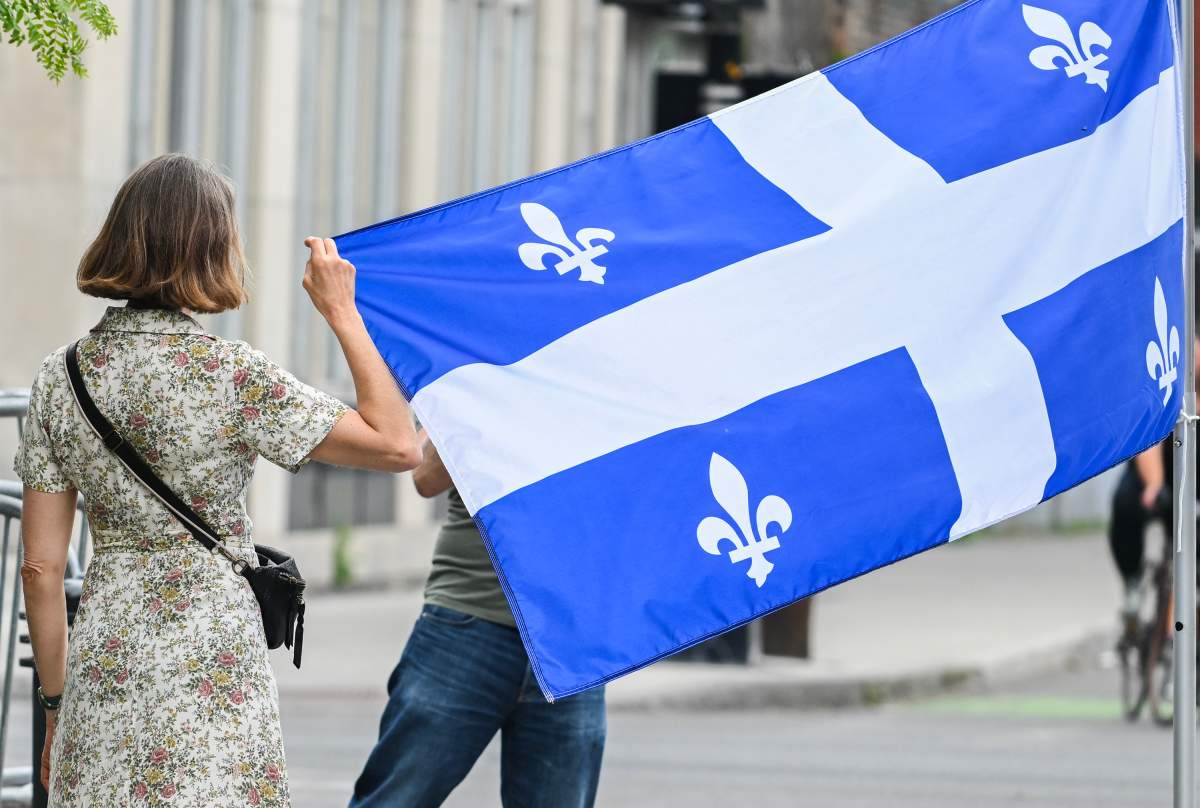 A woman poses next to a Quebec flag on Saint-Jean-Baptiste day in Montreal, Saturday, June 24, 2023.