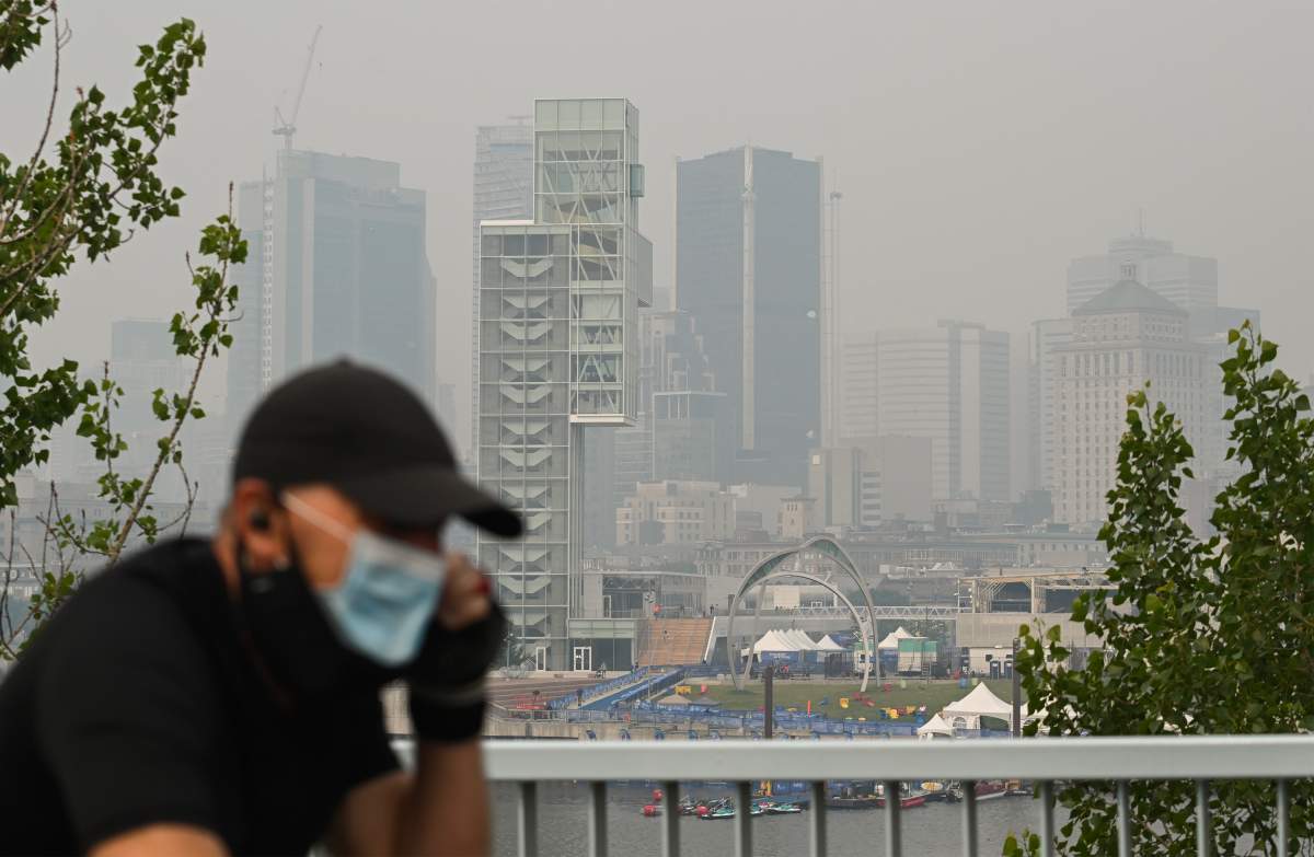 A man wears a face mask as he cycles by the skyline of Montreal, Sunday, June 25, 2023. A smog warning is in effect for Montreal and multiple regions of the province due to forest fires.