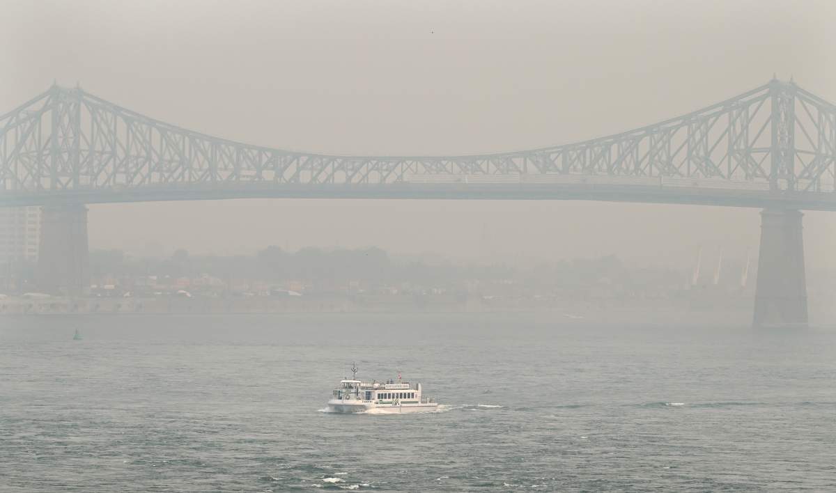 A boat passes by the Jacques Cartier bridge obscured by a haze of smog in Montreal, Sunday, June 25, 2023, as a smog warning is in effect for the city and multiple regions of the province due to forest fires.