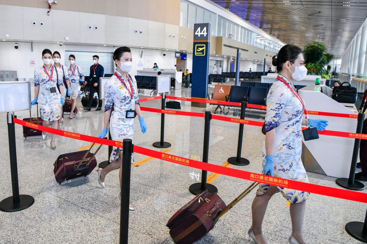 Hainan Airlines flight attendants walk through an airport in uniform. They are carrying luggage.