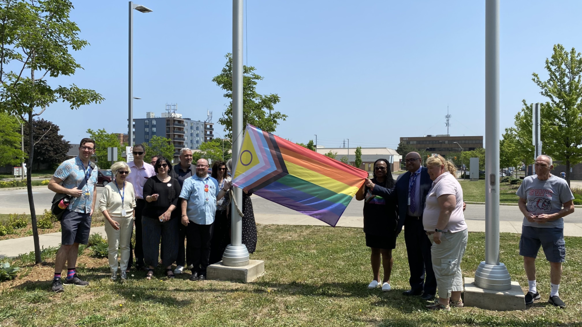 Staff members with the Hamilton-Wentworth District School Board pose in front of the new intersex-inclusive Pride flag that has been raised in front of the board's headquarters.