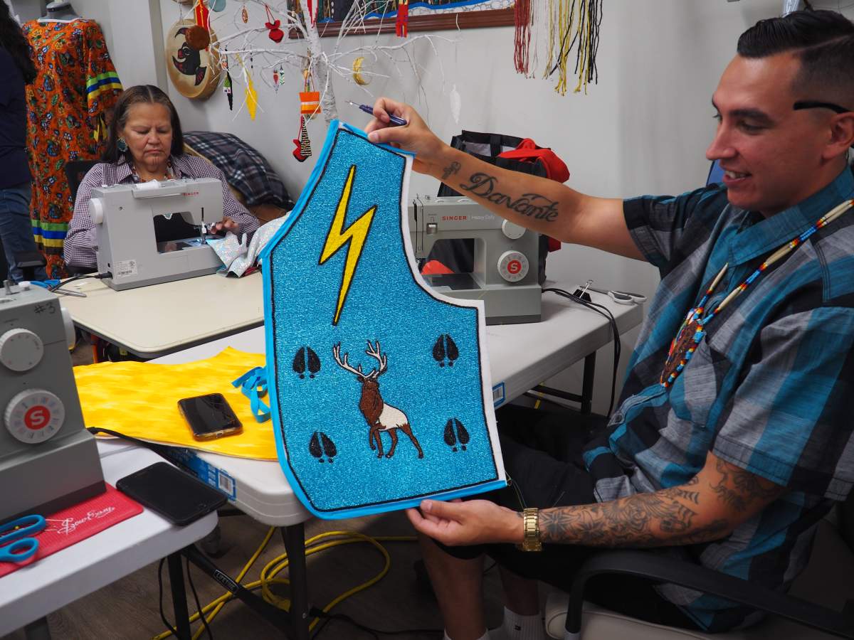 A man holds part of a beaded vest. It is blue with a lightning bolt.