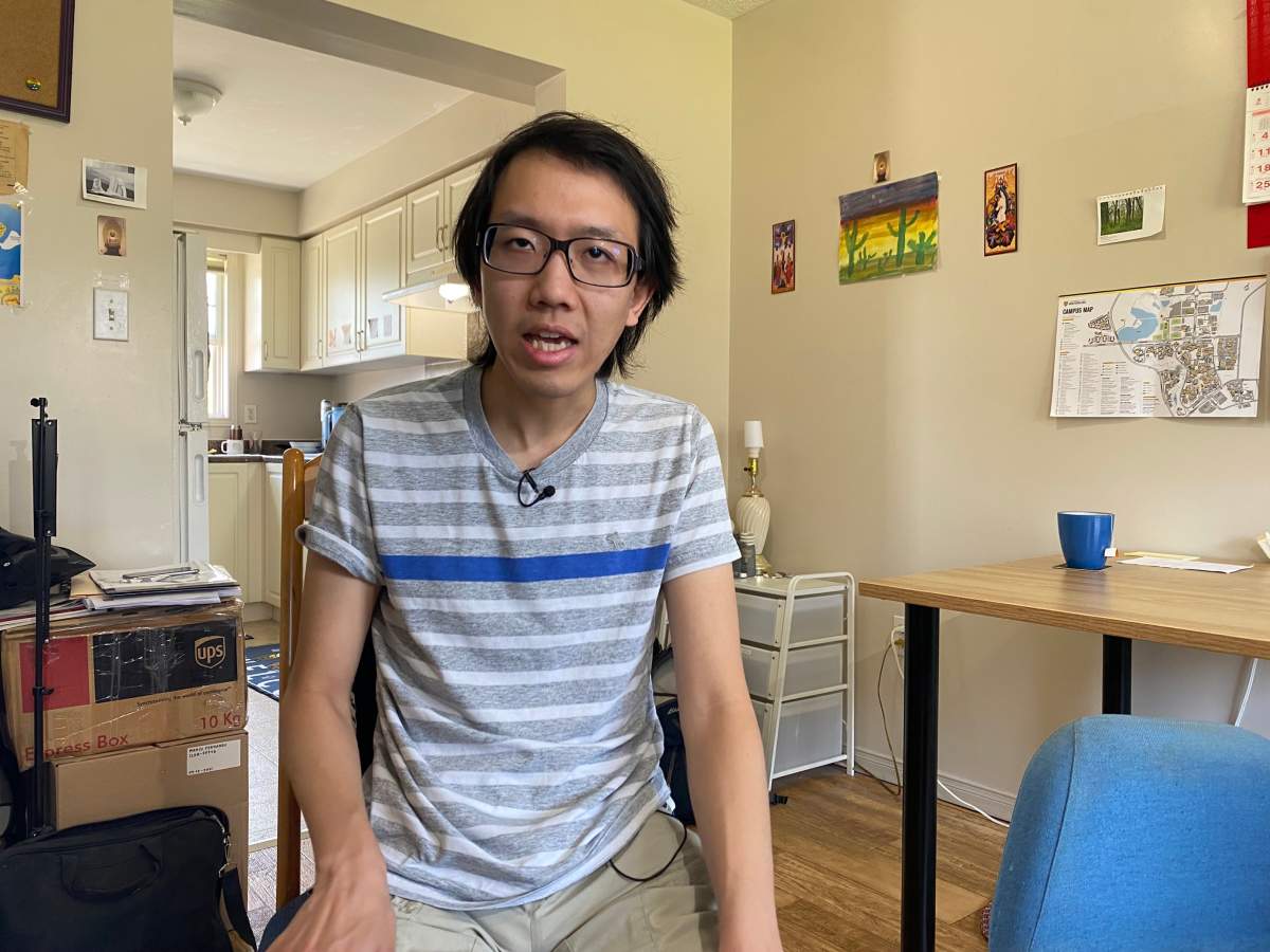 A young man in glasses with dark hair in a striped t-shirt sitting in a residence.