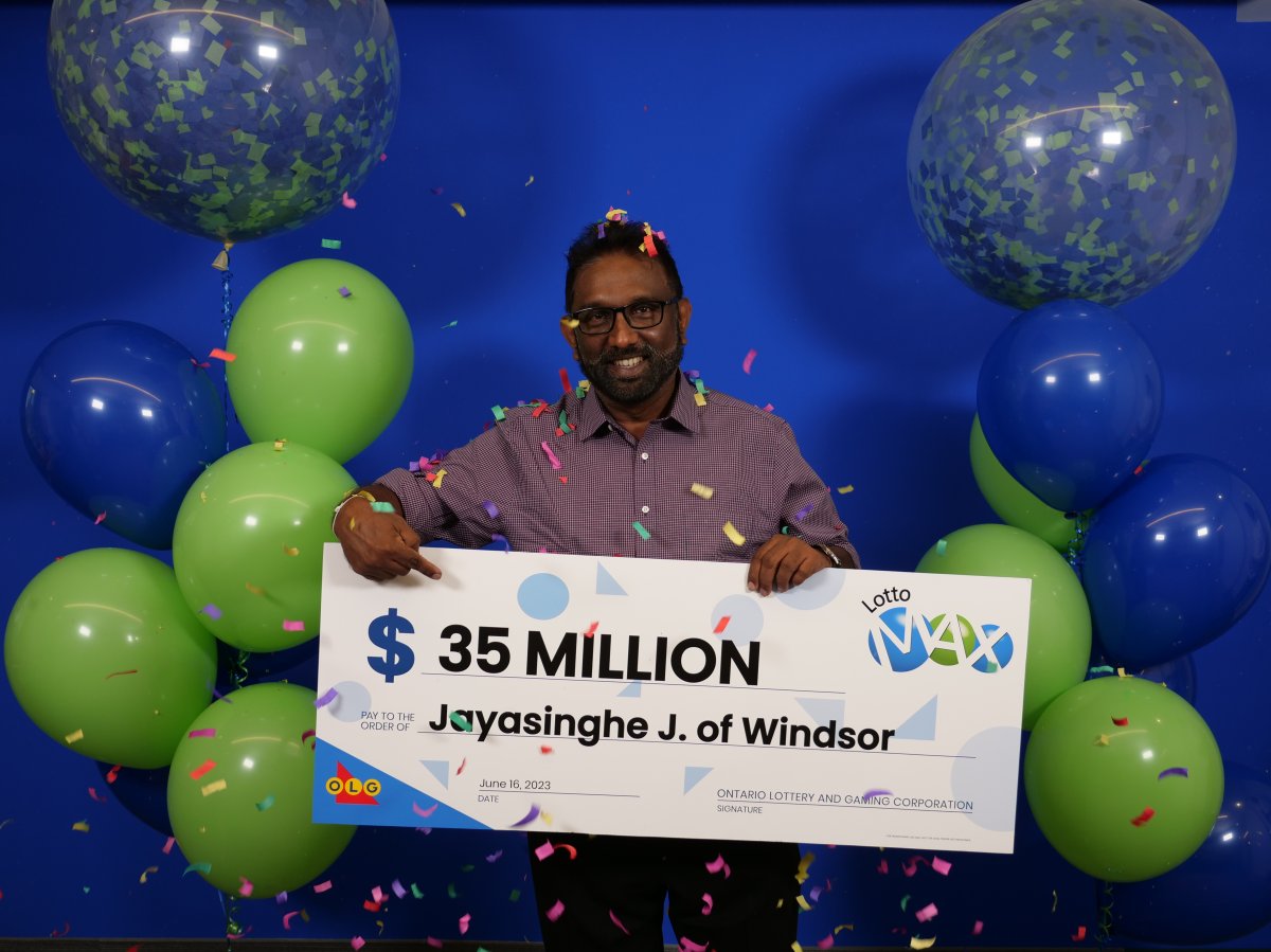 A man posing with a large cheque with confetti and green and blue balloons.