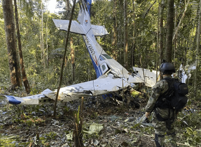 A soldier stands in front of a small, crashed airplane.