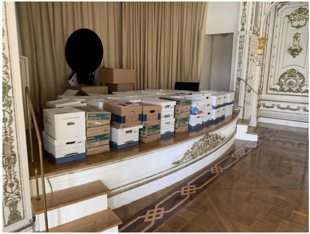 A photo included in a U.S. Department of Justice indictment shows file boxes allegedly containing classified materials stored on the stage of a ballroom at Trump’s Mar-a-Lago resort. The photo is presented as evidence against Trump and his alleged mishandling and withholding of classified materials after he left the White House in 2021.