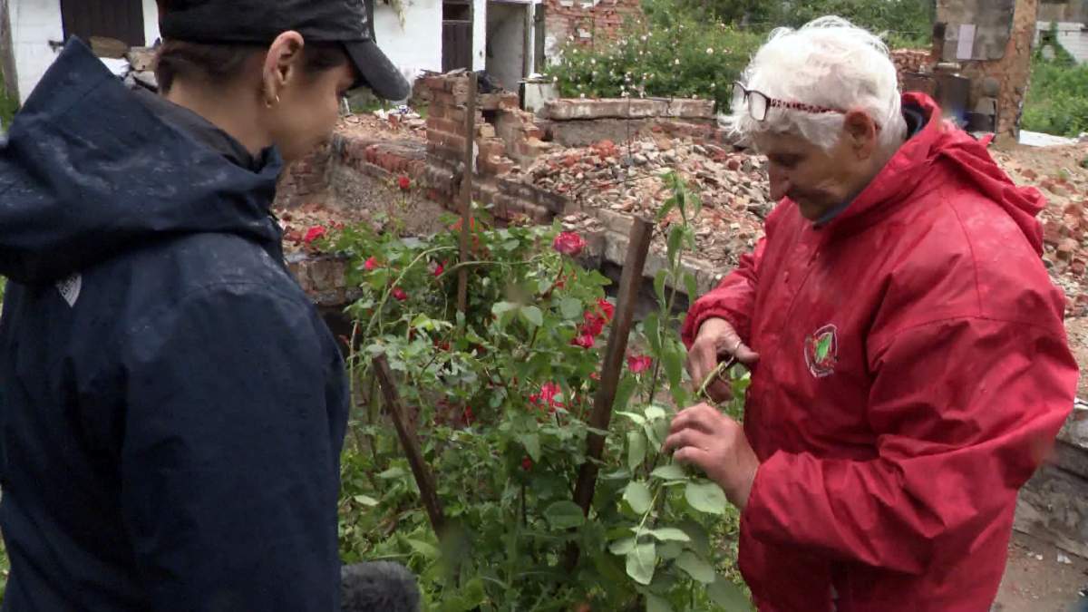 A woman in a red coat cuts roses left blooming beside the ruins of her home in Ukraine.