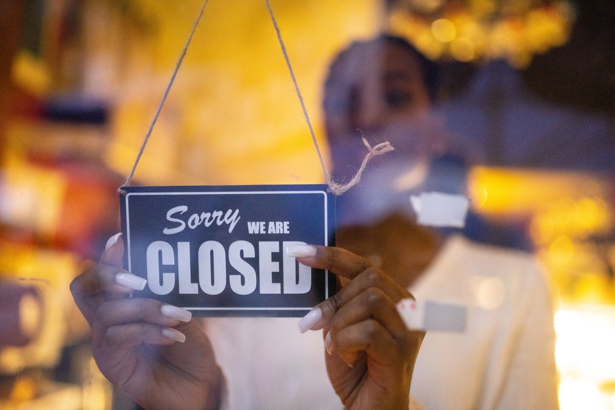A woman behind a door holding a sign that says "Sorry we're closed".