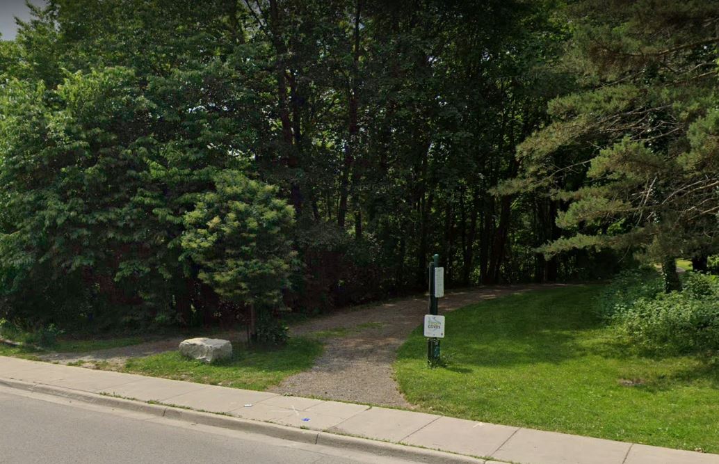 The entrance to a wooded area from a road and sidewalk in London, Ont.