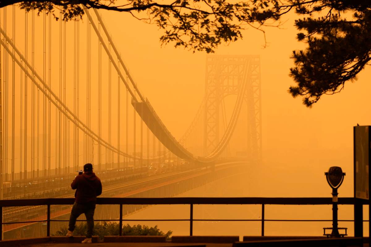 A man talks on his phone as he looks through the haze at the George Washington Bridge from Englewood Cliffs, N.J., Wednesday, June 7, 2023. Intense Canadian wildfires are blanketing the northeastern U.S. in a dystopian haze, turning the air acrid, the sky yellowish gray and prompting warnings for vulnerable populations to stay inside. (AP Photo/Seth Wenig)