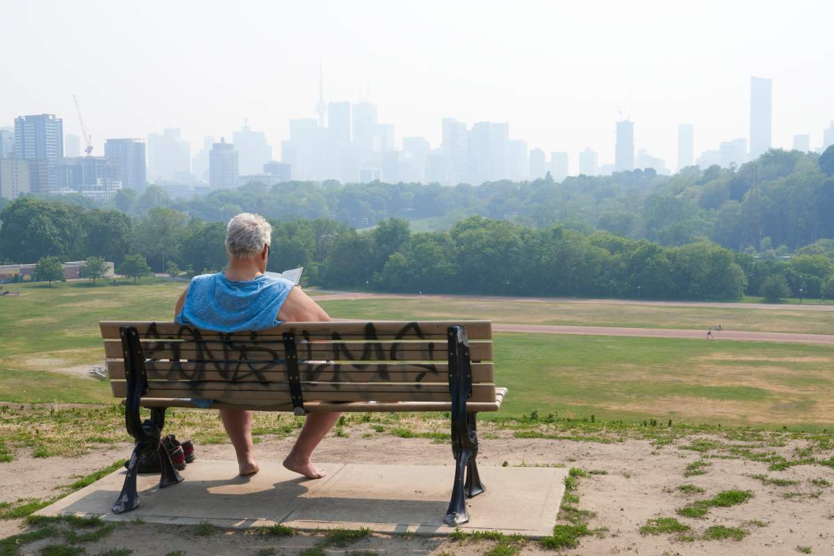 A person sits on a bench overlooking Riverdale Park East in Toronto on Tuesday, as the city remains under a special air quality statement caused by forest fires. THE CANADIAN PRESS IMAGES/Rachel Verbin