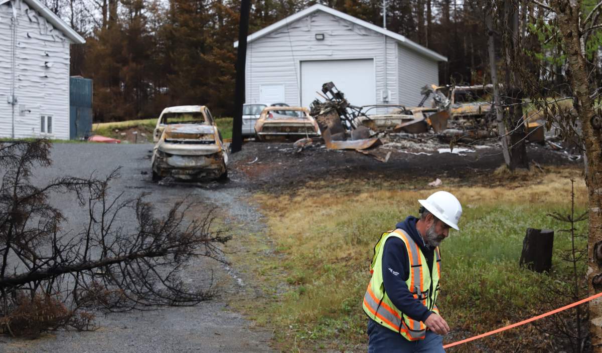 A Halifax Water employee walks past a property with fire damaged cars, on Yankeetown Road in Hammonds Plains, N.S. Tuesday June 6, 2023.