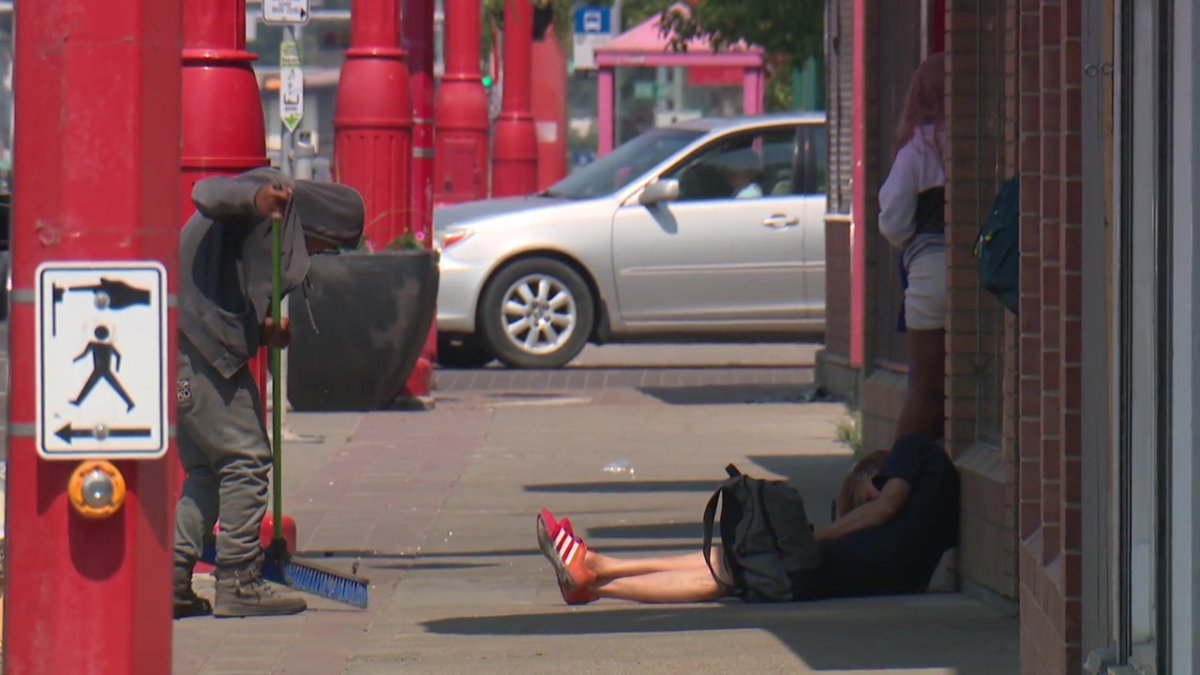 A man sweeps in Edmonton's Chinatown while a person sits on the sidewalk.