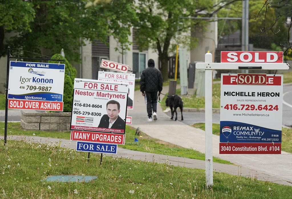 A person walks past multiple for-sale and sold real estate signs in Mississauga, Ont., Wednesday, May 24, 2023. 