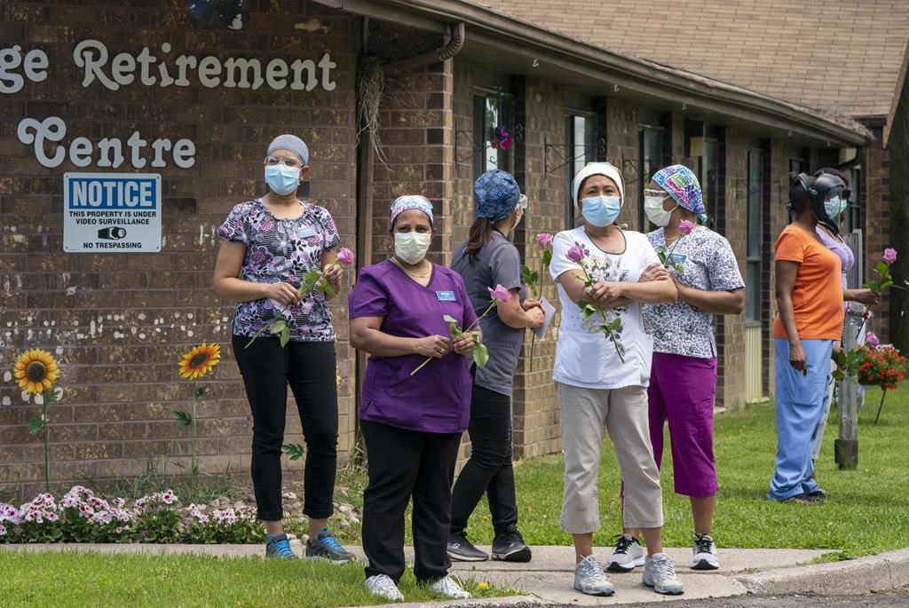 Workers hold flowers given to them as they watch as 150 nursing union members show support at Orchard Villa Long-Term Care in Pickering, Ont. on Monday, June 1, 2020. THE CANADIAN PRESS/Frank Gunn.