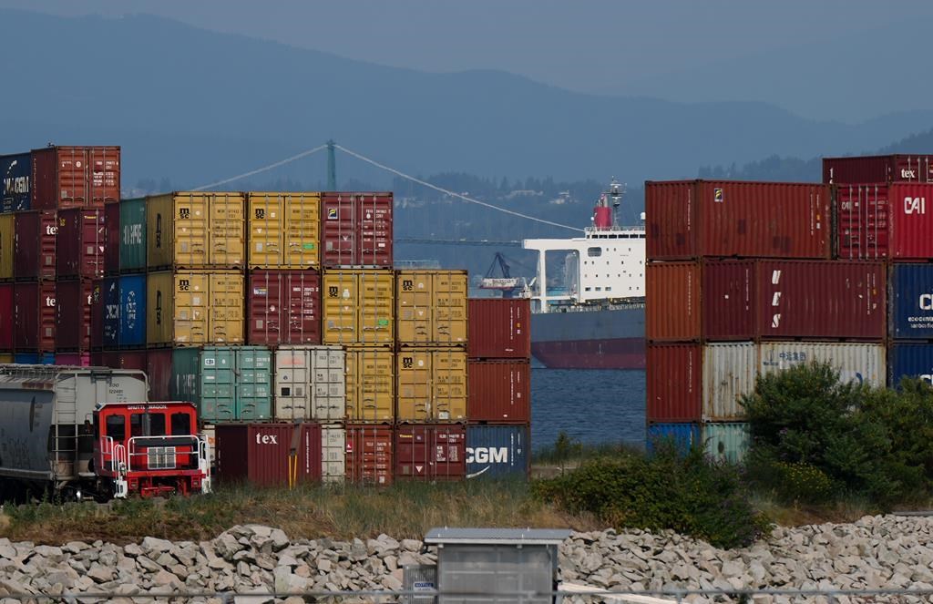 A freighter sits at anchor on the harbour as cargo containers are seen stacked at port during a strike by International Longshore and Warehouse Union Canada workers, in Vancouver, B.C., Tuesday, July 4, 2023.