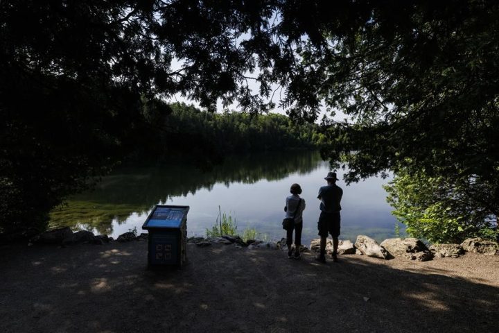 People look out on the water from the shore of Crawford Lake in Milton, Ont., on Friday, July 7, 2023.