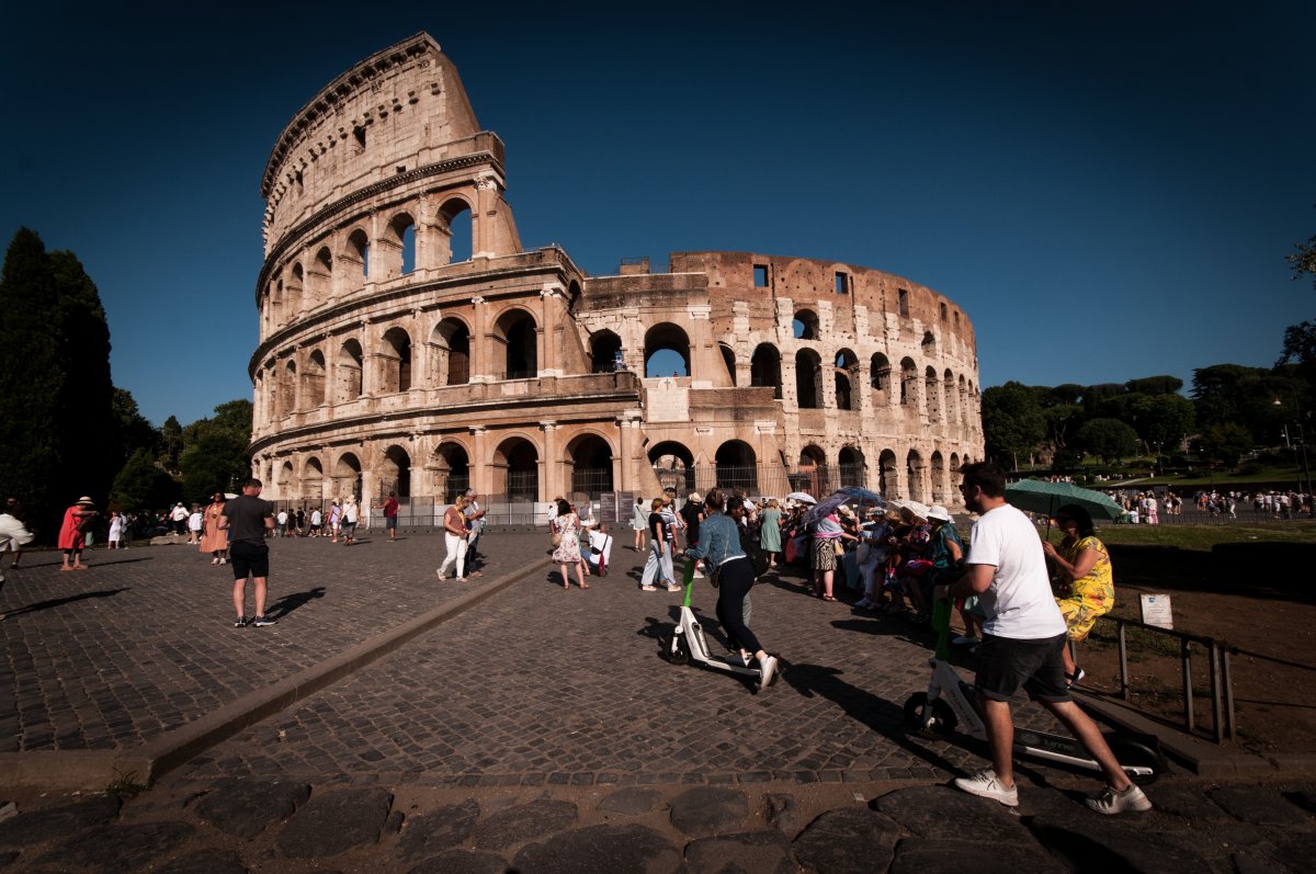 The Colosseum in daylight. Groups of people stand on the streets in front of the Colosseum.