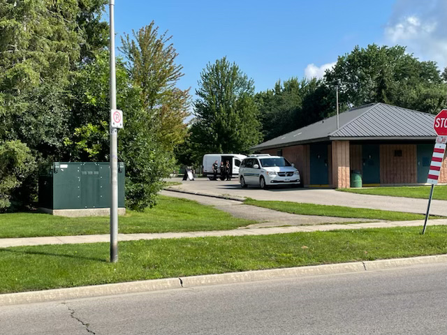 The entrance to a park on a sunny day with a police van parked next to a park building.