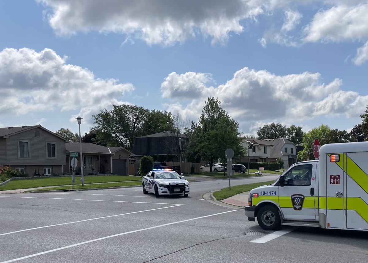 An ambulance and police cruiser at a residential intersection on a summer day.